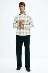 Sobrecamisa de franela con cuello inglés, tapeta lisa, dos bolsillos superiores con solapa y mangas largas con puños abotonados. Presenta un patrón de cuadros en tonos blanco y beige/tostado.