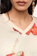 Blusa de corte oversize color beige, con estampado artístico de personas en movimiento de tonos rojos, escote en V y mangas cortas.