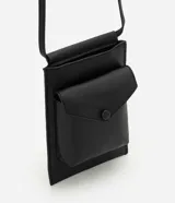 Billetera crossbody de poliuretano color negro, de diseño compacto y moderno con compartimento principal y bolsillo frontal con solapa y cierre a presión. Cuenta con asa larga para uso cruzado.
