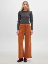 Pantalón ancho y suelto de tejido tipo terciopelo color naranja, con cintura elástica y cordón ajustable. Presenta detalles de pespuntes decorativos a los lados.