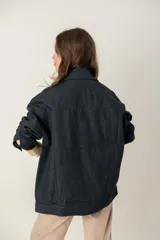 Campera de jean oversize color negro, con corte largo, cuello camisero, cierre frontal con botones metálicos y bolsillos frontales. Presenta un parche de cuero con logo en el pecho.