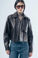 Chaqueta de cuero sintético en color marrón oscuro, con cuello clásico, cierre frontal con botones a presión y dos bolsillos aplicados en el pecho. Presenta un corte recto y estructurado.
