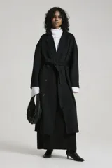 Tapado largo negro con cuello solapa, doble botonadura, cinturón y bolsillos laterales.