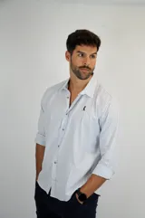 Camisa de manga larga con diseño de rayas verticales finas en tonos claros. Presenta cuello clásico, cierre frontal con botones y un pequeño logo bordado en el pecho.