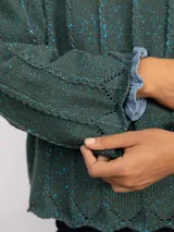 Sweater de punto oversize en color bordó con destellos de lurex. Presenta un diseño acanalado vertical, cuello redondo y mangas largas con terminaciones acampanadas y bordes ondulados.