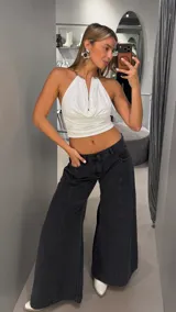 Top halter blanco con escote drapeado y argollas metálicas en los tirantes.