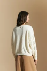 Cardigan de punto color terracota con diseño de trenzas verticales, cuello redondo y cierre frontal con botones metálicos. Presenta mangas largas con puños ajustados y un calce holgado.