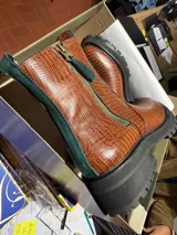 Bota de cuero con textura tipo crocco en color caramelo, con suela track negra y detalles de cierre lateral y ribetes en color rojo.