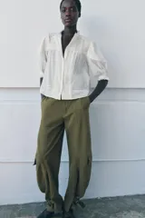 Camisa blanca de algodón con cuello redondo y manga por debajo del codo abullonada. Presenta detalles de bordados a tono y cierre frontal con botones.