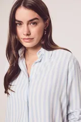 Camisa oversize celeste y blanca a rayas verticales, de mangas largas con puños abotonados y cuello camisero.