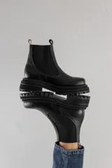 Botas tipo chelsea de cuero negro con textura granulada, paneles laterales elásticos y suela track robusta de goma.