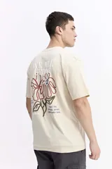 Remera de manga corta color crema con cuello redondo y fit regular. Presenta un estampado grande en la espalda con una flor estilizada en tonos rojo y azul, y texto que incluye "WE ALL GROW" y "trust the process, great things take time".