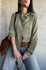 Camisa de manga larga color verde militar con inserciones de encaje decorativo en el frente y las mangas, cuello camisero y cierre frontal de botones.