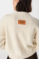 Sweater de punto color crudo con cuello alto y mangas largas abullonadas. Presenta apliques de cuero marrón en forma de rombos en los codos.