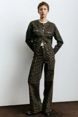 Campera corta de denim con estampado de leopardo en tonos marrón y negro. Diseño sin cuello (tipo 'collar mao') con cierre frontal de botones metálicos plateados y cuatro bolsillos frontales de parche con botón.