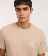 Remera masculina de algodón color beige, modelo comfort, con cuello redondo y manga corta. Presenta un pequeño estampado cuadrado en el pecho con un diseño de sol estilizado.