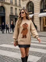 Sweater de punto color marrón claro, con diseño de oso estampado en el frente. Presenta cuello redondo, mangas largas con puños ajustados y corte holgado.