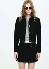 Chaqueta corta de corte recto y diseño crop, con cuello camisero y cierre frontal de botones metálicos. Presenta manga larga y forro interior.