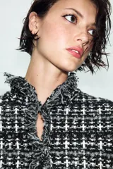 Chaqueta de punto con textura, cuello redondo y manga larga. Presenta detalles de acabados deshilachados en los bordes y cierre frontal con ganchos.