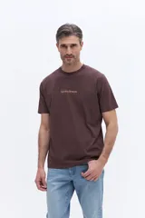 Remera de manga corta color marrón chocolate, con cuello redondo y calce regular. Presenta un pequeño estampado gráfico en el centro del pecho con la inscripción 'Sunday Brunch'.