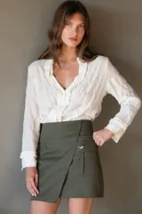 Falda corta color verde militar, estilo wrap o cruzada, con un bolsillo tipo parche con fuelle y un botón decorativo en el frente.