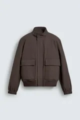 Cazadora regular fit de tejido técnico color marrón, con cuello subido, bolsillos de plastrón con solapa en la cadera, mangas largas con puños elásticos y cierre frontal con cremallera oculta por solapa con botones a presión.