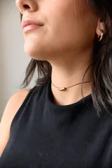 Gargantilla minimalista compuesta por un hilo encerado fino y un dije central de acero quirúrgico en forma de tubo curvo.