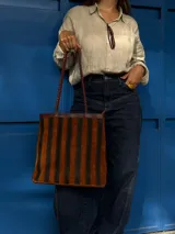 Cartera tipo tote de cuero con diseño de franjas verticales multicolores en tonos tierra, rojo y azul. Cuenta con correas trenzadas de cuero y cierre superior.