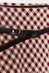 Falda midi de tiro alto con estampado de cuadros vichy en tonos burdeos y beige. Presenta cintura elástica y un cinturón fino de cuero negro con hebilla metálica.