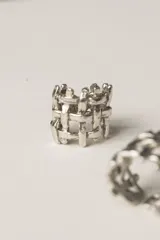Anillo de diseño abierto con estructura de rejilla entrelazada, elaborado artesanalmente en metal con acabado plateado.