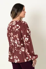 Blusa color marrón con estampado de flores blancas, de manga larga abullonada con puño elástico y cuello redondo con detalle de frunces horizontales.
