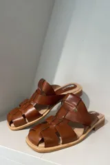 Zuecos negros de cuero charol con diseño de tiras entrecruzadas y suela plana.