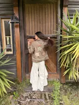 Campera de jean marrón suave con apliques de flores de crochet en el pecho, costuras decorativas artesanales en cuello y bordes, bolsillos frontales y cierre con botones.