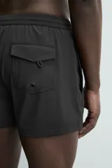 Short de baño negro de tejido técnico con estructura ripstop resistente a desgarros, cintura ajustable con cordón y bolsillos laterales.