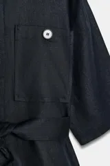 Chaqueta de estilo safari confeccionada en mezcla de lino, color azul marino, con cuello solapa, mangas cortas y cierre frontal con botones ocultos. Presenta bolsillos de parche en el pecho con solapa y botones, además de un cinturón ajustable del mismo tejido para anudar en la cintura.