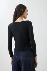 Remera de manga larga, color blanco roto, con cuello bote y textura acanalada. Presenta un efecto de doble capa o transparencia sutil en el escote.