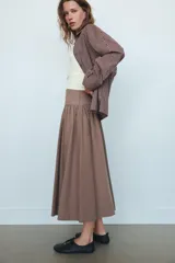 Camisa de manga larga con cuello solapa y diseño de cuadros pequeños. Presenta mangas con pliegues y cierre frontal con botones ocultos.