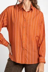 Camisa oversize color ladrillo con rayas verticales blancas y rosadas, de mangas largas y botones de madera.