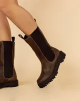 Bota de cuero color chocolate, de caña alta con elásticos laterales y tiradores en la parte superior. Suela de neolite color negro. Diseño artesanal fabricado en Uruguay.