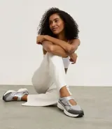 Championes de estilo híbrido entre jogging y Mary Jane, confeccionados en poliuretano. Presentan un diseño con cierre de tira adherente en el empeine, suela robusta y detalles en tonos grises y plateados.