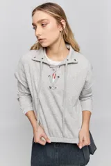 Buzo de calce relajado color tostado, con cuello alto y detalle de cordones entrelazados con ojales metálicos en el frente. Posee bolsillos laterales ocultos y puños y ruedo elastizados.