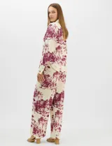 Conjunto de dos piezas compuesto por camisa de manga larga con cuello solapa y botones frontales, y pantalón de tiro alto con pierna recta y bolsillos laterales. Ambas prendas presentan un estampado paisajístico en tonos marrones sobre fondo crema.