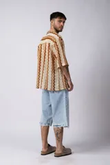 Camisa de manga corta con cuello solapa, confeccionada en tejido de punto crochet con patrón ondulado en tonos marrón y beige.