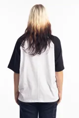 Remera de corte oversize con diseño tipo ranglan, que combina cuerpo blanco con mangas y cuello en color negro. Presenta un pequeño logo bordado en el centro del pecho.
