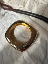 Brazalete rígido de diseño cuadrado con acabado metálico brillante en tono dorado.