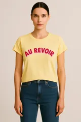 Remera amarilla de manga corta y cuello redondo, con estampa frontal que dice "AU REVOIR" en color rojo con borde rosado.