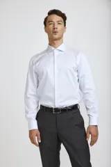 Camisa de vestir blanca de corte clásico, con cuello rígido, cierre frontal de botones y mangas largas con puños abotonados.