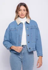 Campera de jean celeste con cuello y forro de corderito color crema, corte cuadrado, cierre frontal con botones metálicos, dos bolsillos de parche en el pecho y elástico en el ruedo.