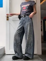 Jean wide leg de tiro alto en denim azul oscuro, con aplicaciones brillantes verticales en toda la prenda. Presenta un calce relajado y oversize.