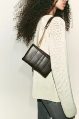 Bolso mini bandolera de efecto acolchado, color marrón oscuro, con pespuntes verticales. Posee asa de cadena dorada que puede usarse como doble asa de hombro. Cierre mediante solapa y botón imantado.